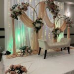 Gold wedding arch with peach fabric and pink roses before a white curtain backdrop