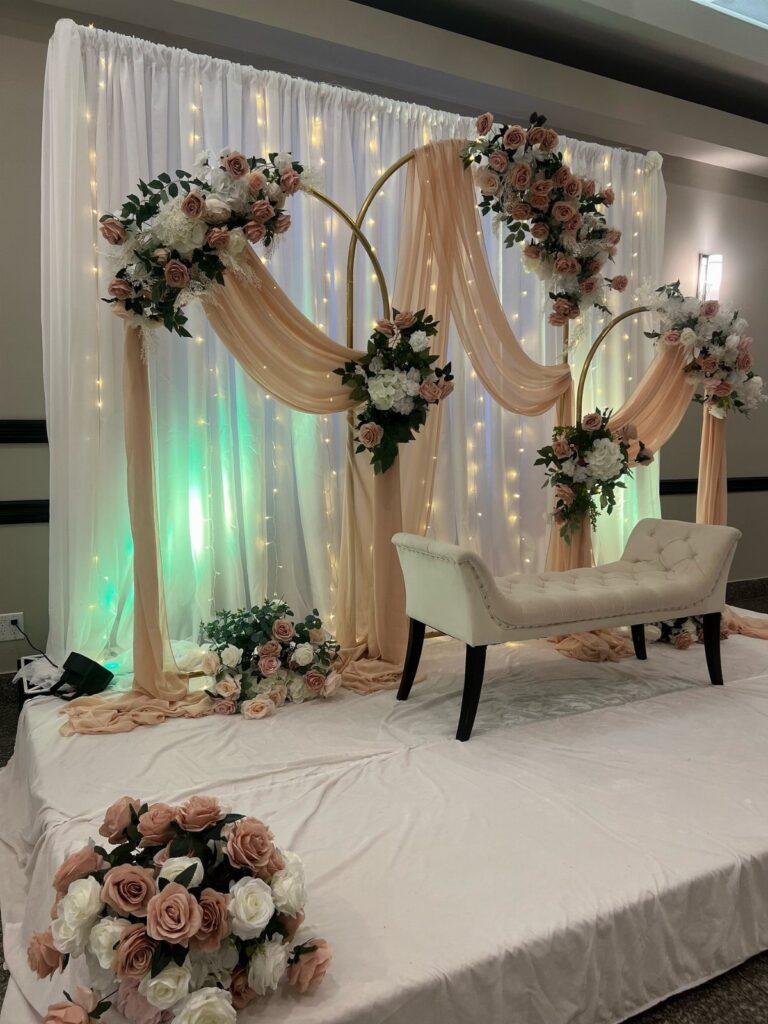 Gold wedding arch with peach fabric and pink roses before a white curtain backdrop