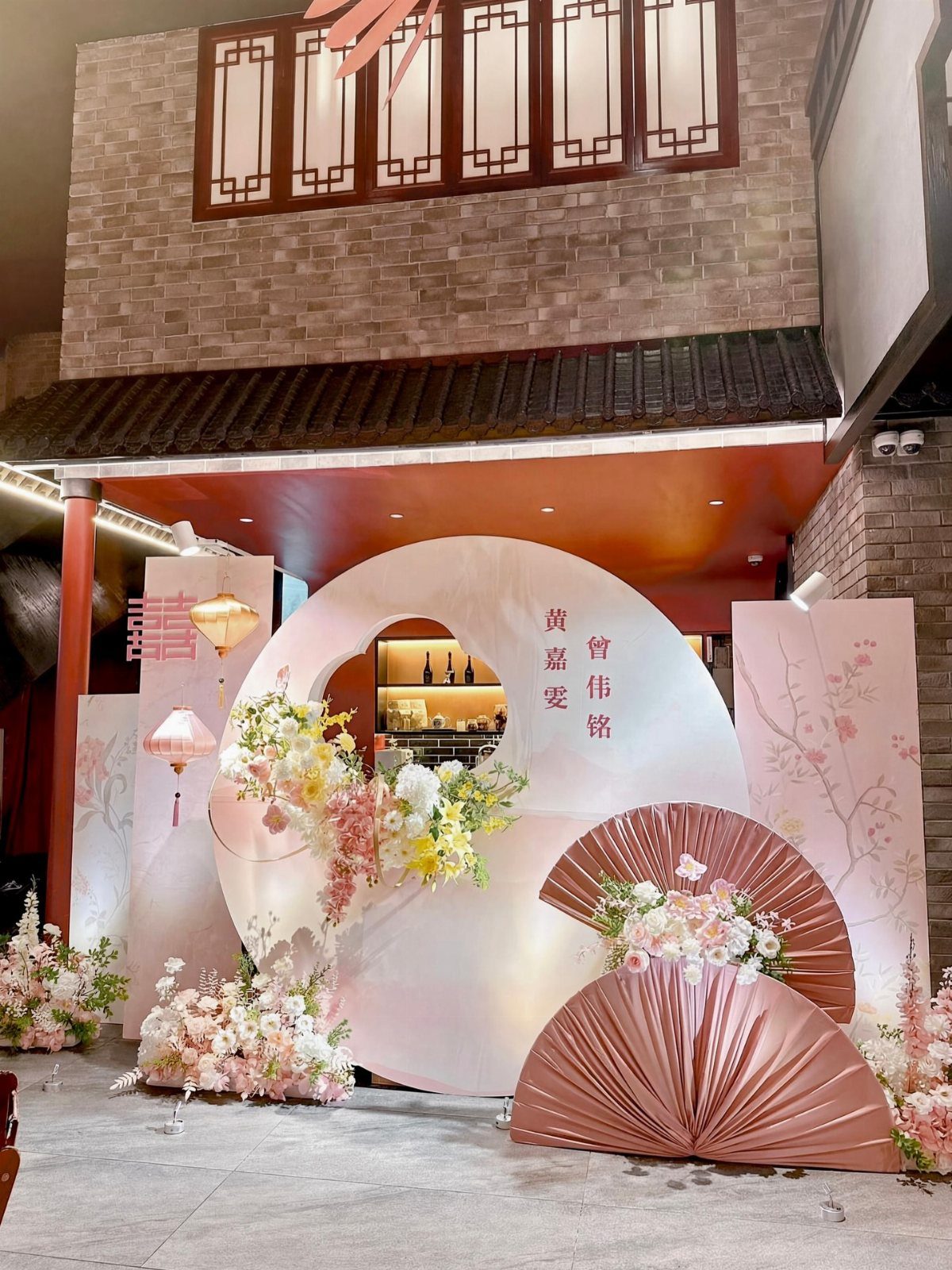 Chinese wedding decor featuring a circular backdrop, pink fans, and floral arrangements.