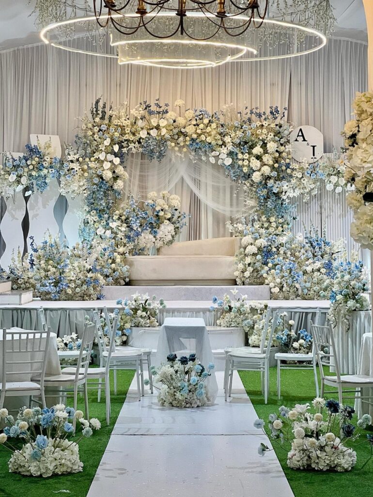 Wedding ceremony setup with white chairs and a large dusty blue floral arch.