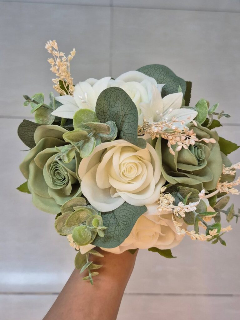 Green wedding bouquet with cream roses and succulents held by a hand.