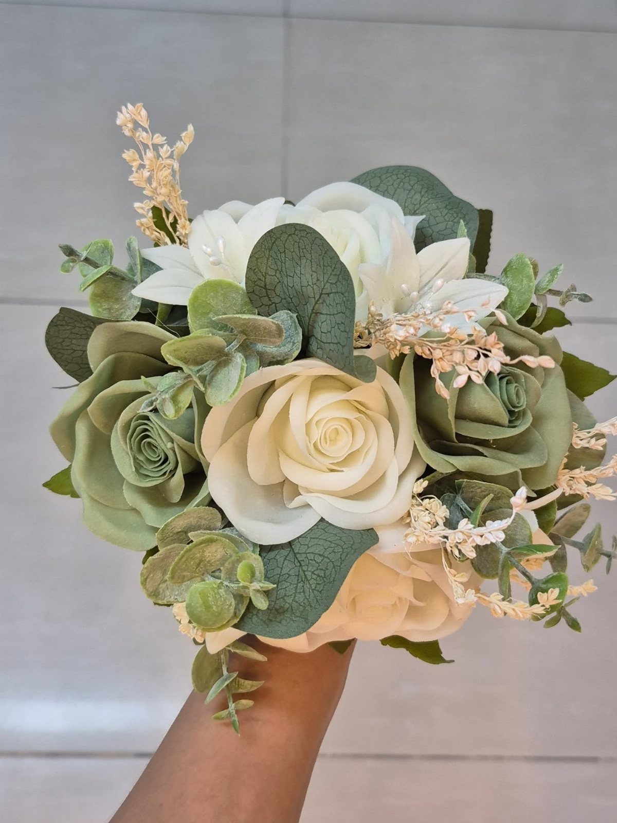 Green wedding bouquet with cream roses and succulents held by a hand.