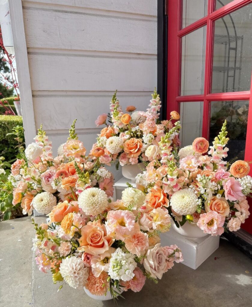 Blush pink and peach floral arrangements in white pots on a porch.