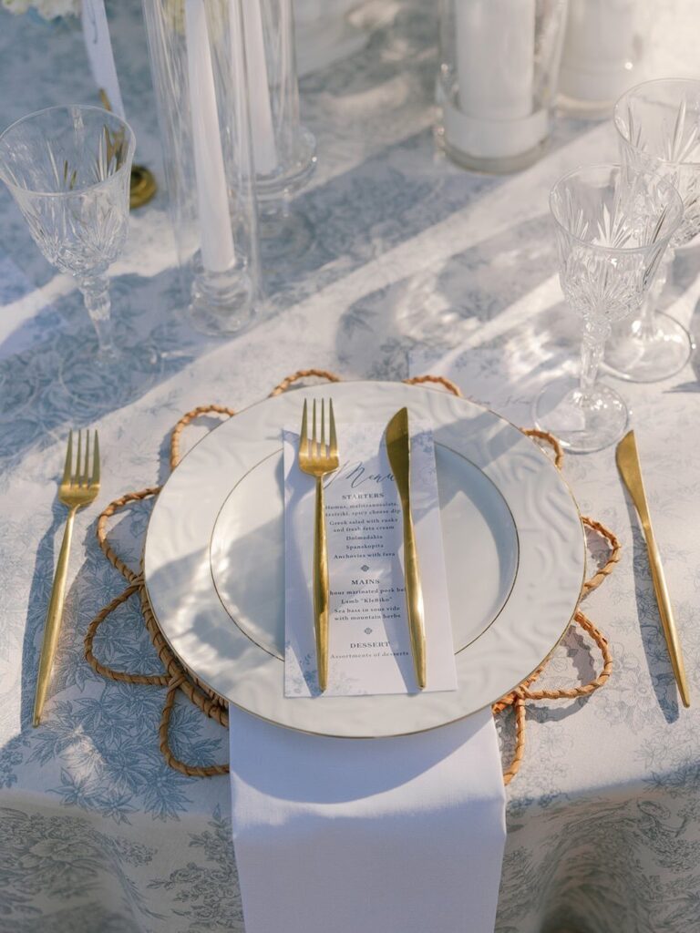 Wedding table setting with light blue tablecloth, white plates, and gold cutlery.