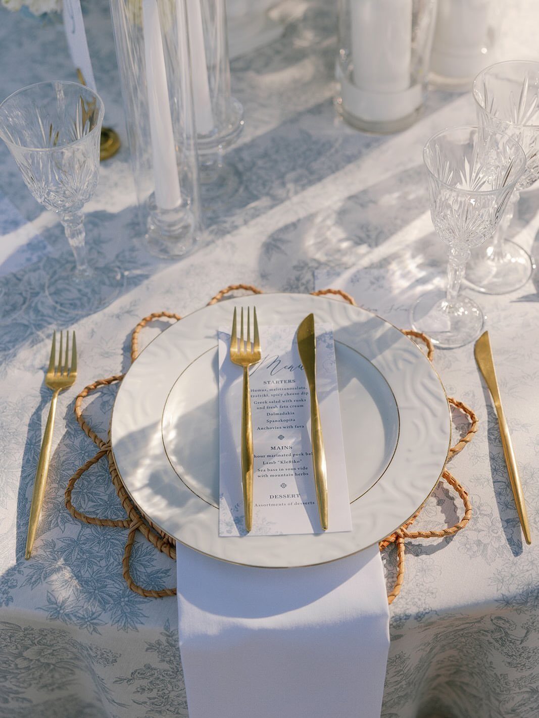 Wedding table setting with light blue tablecloth, white plates, and gold cutlery.