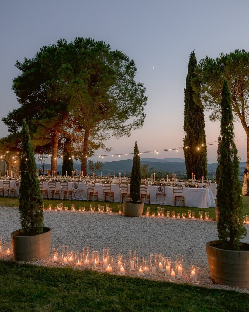 Long wedding table with white linens and candles outdoors under string lights