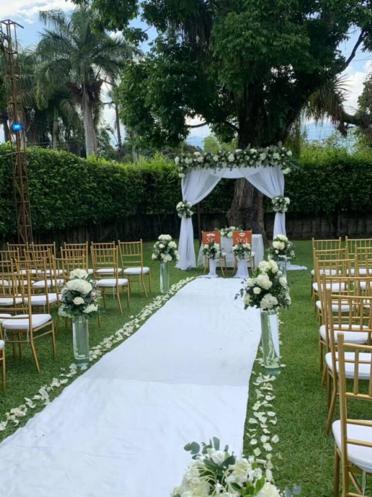 Outdoor wedding ceremony setup with white floral arch and gold chairs on green grass