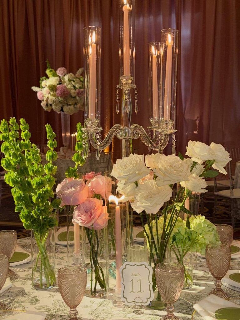 Wedding table centerpiece with pink and white roses, green flowers, and lit candles.