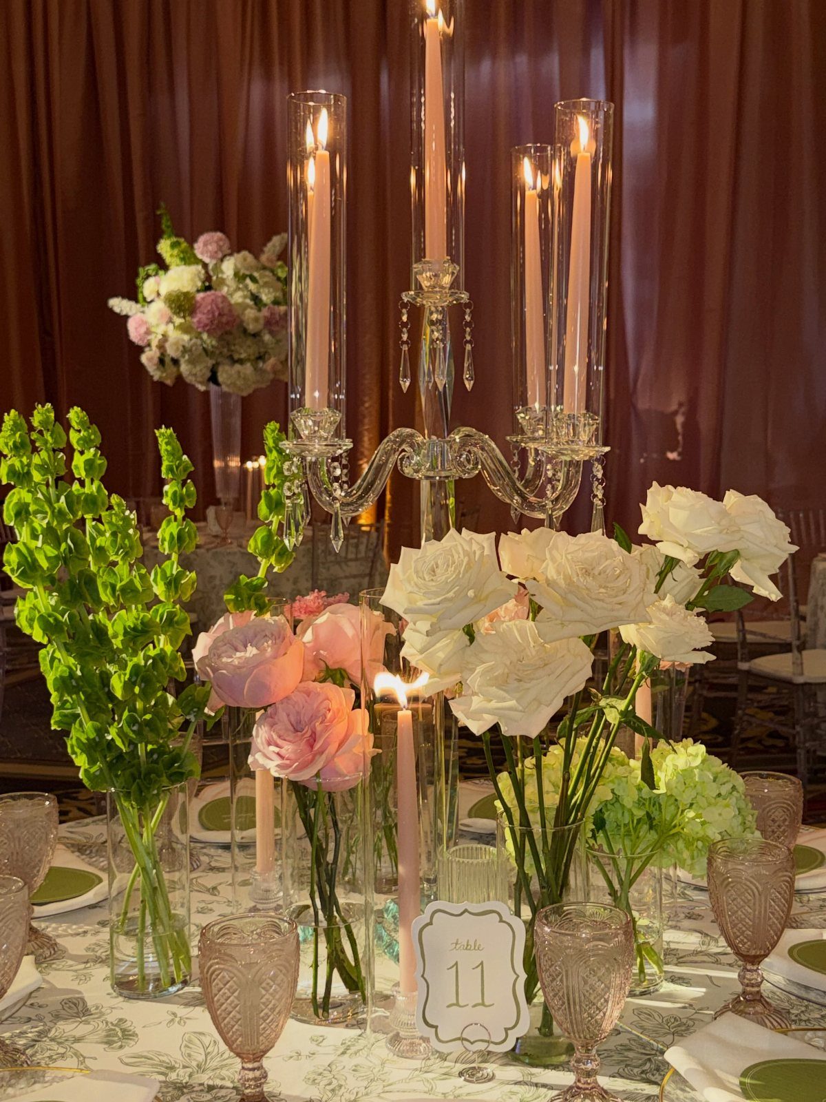 Wedding table centerpiece with pink and white roses, green flowers, and lit candles.
