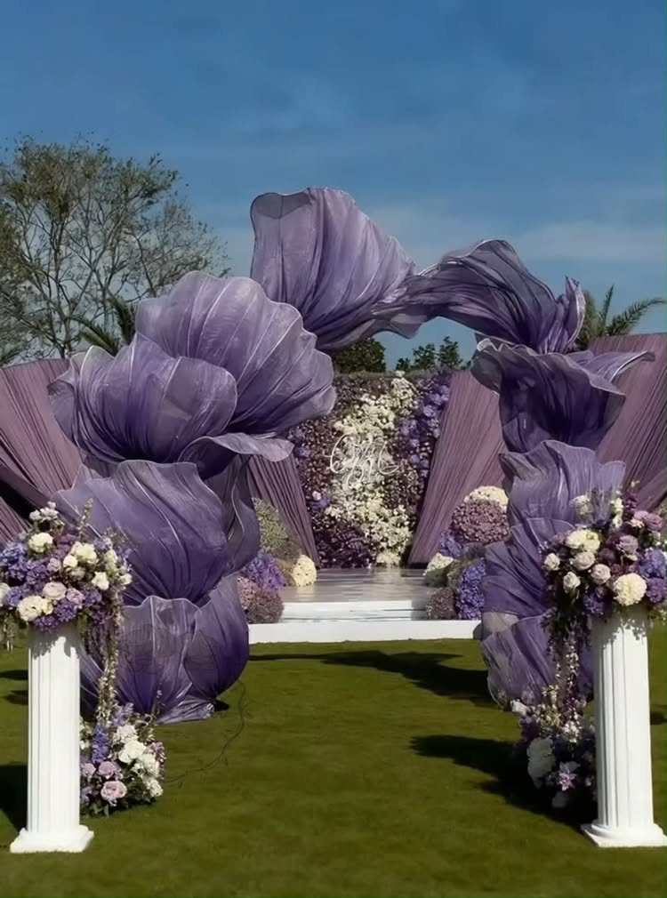 Purple fabric petal arch and floral arrangements at an outdoor wedding ceremony venue