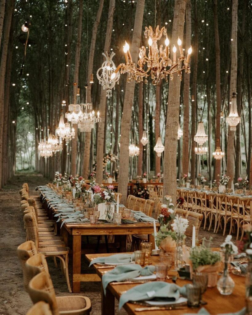 Wooden reception tables with floral arrangements and crystal chandeliers in a forest setting