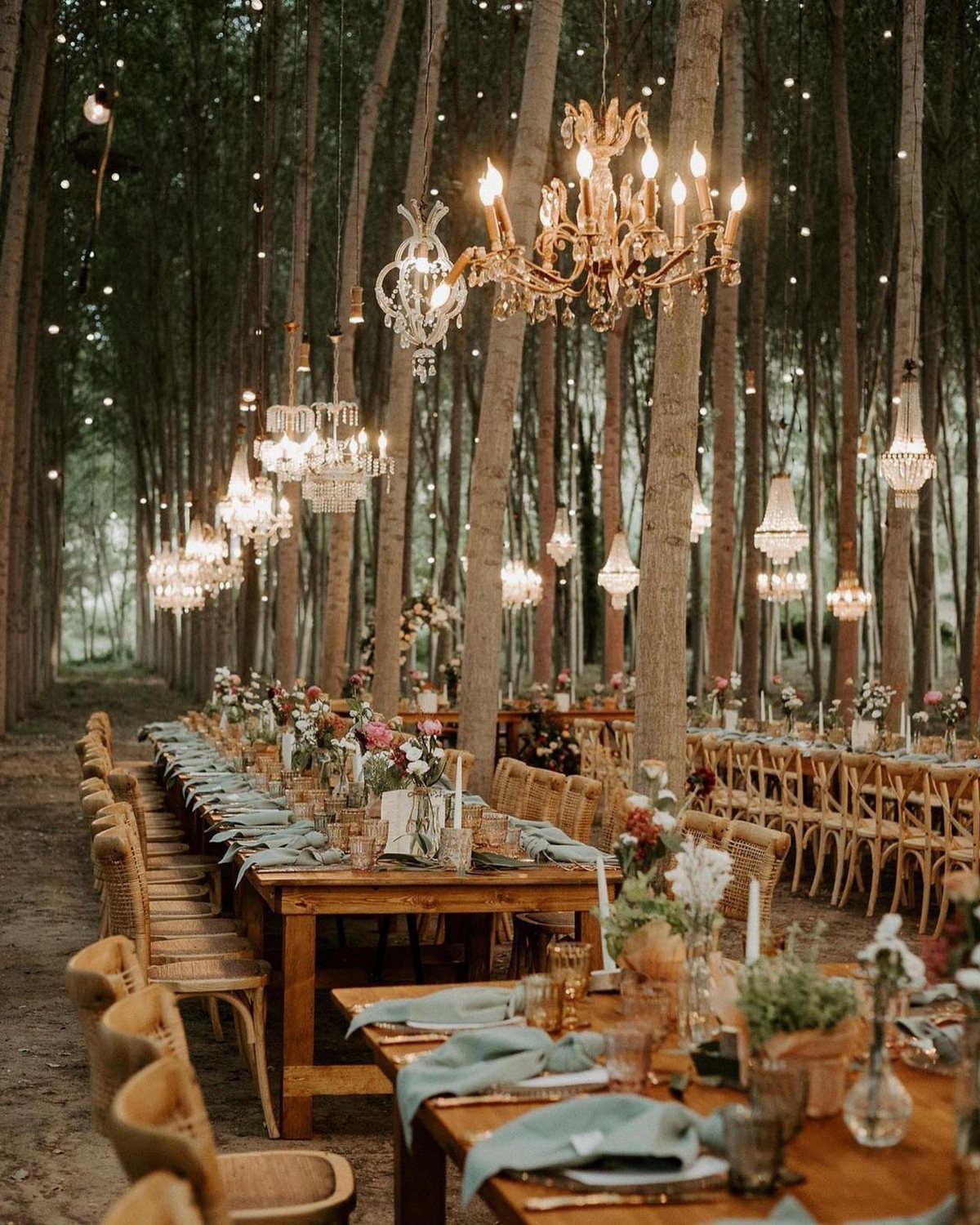 Wooden reception tables with floral arrangements and crystal chandeliers in a forest setting