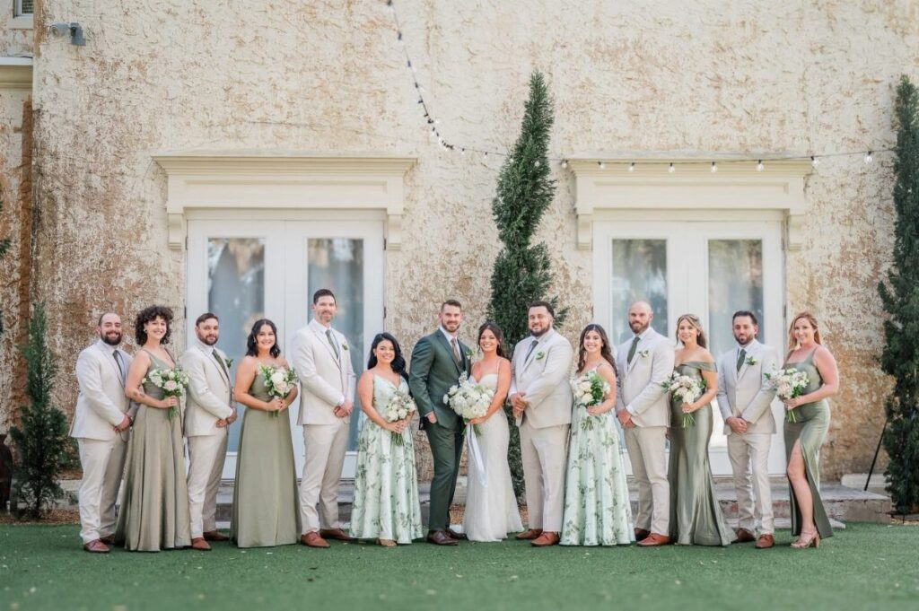 Wedding party posing outdoors with bridesmaids in sage green dresses and groom in sage suit.