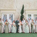 Wedding party posing outdoors with bridesmaids in sage green dresses and groom in sage suit.