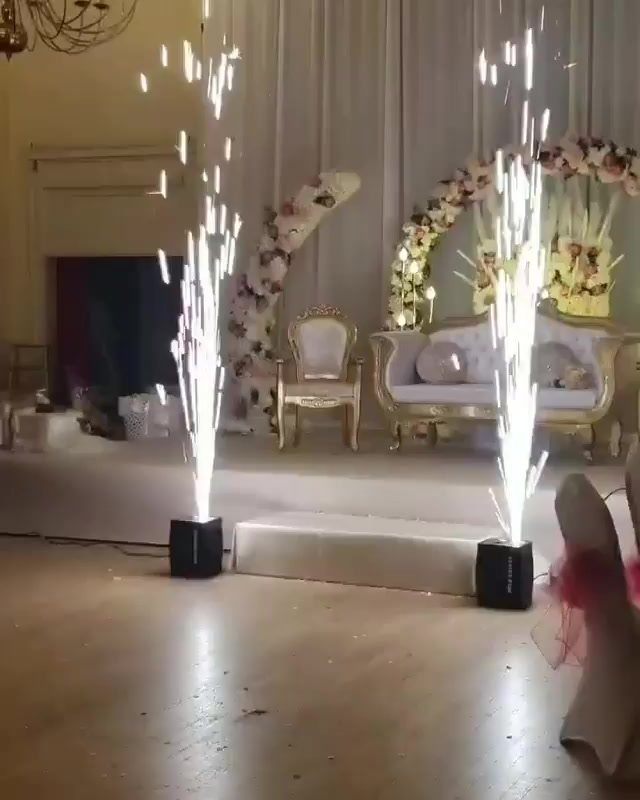 Cold sparkler machines emitting bright white sparks on a wedding stage with floral decor.