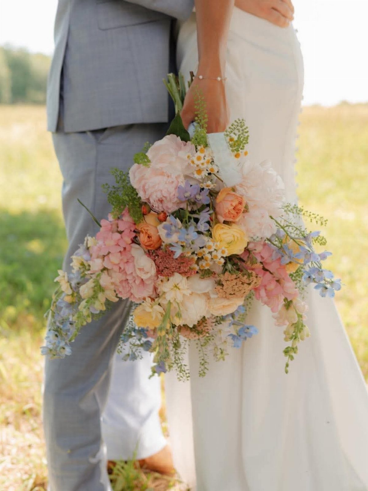 Colorful summer wedding bouquet held by a bride and groom in a sunny field