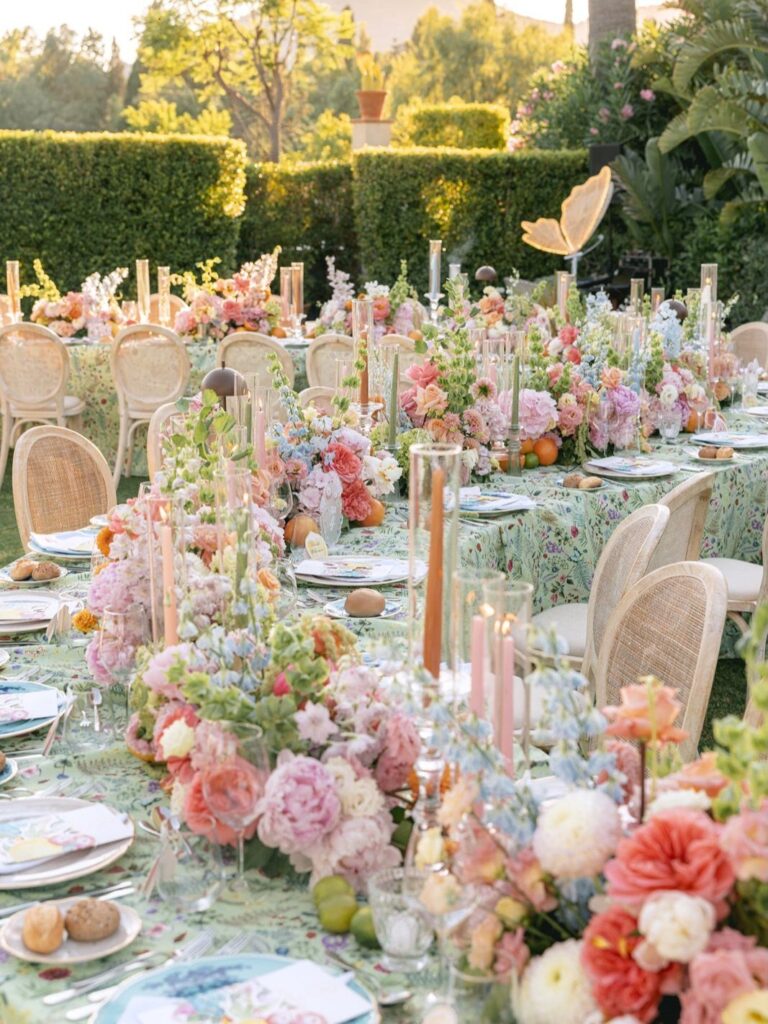 Floral wedding table setting with pink and peach flowers and cane-back chairs outdoors.