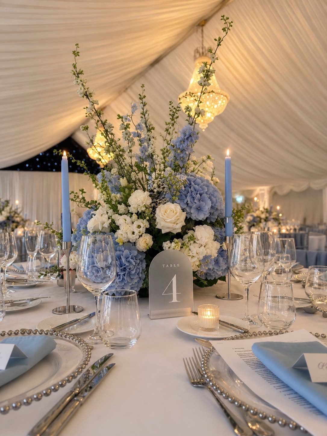 Powder blue wedding table setting with hydrangea centerpiece, blue candles, and silver chargers.
