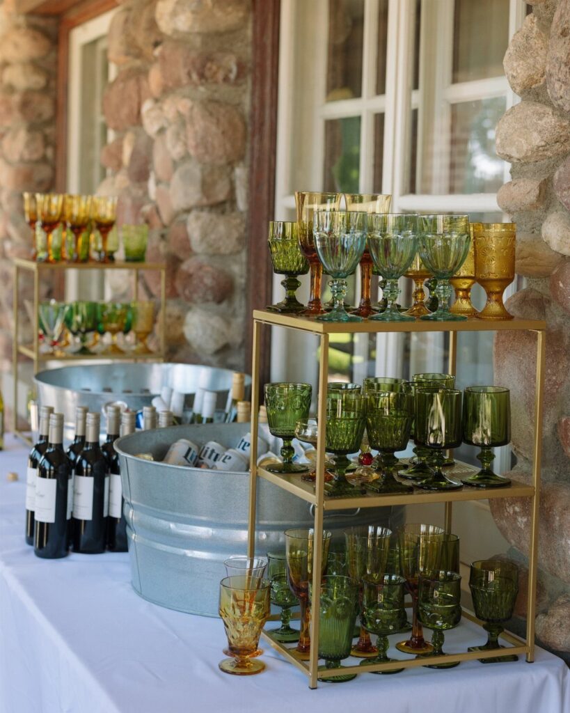Colored vintage glassware arranged on a gold tiered shelf next to wine bottles.