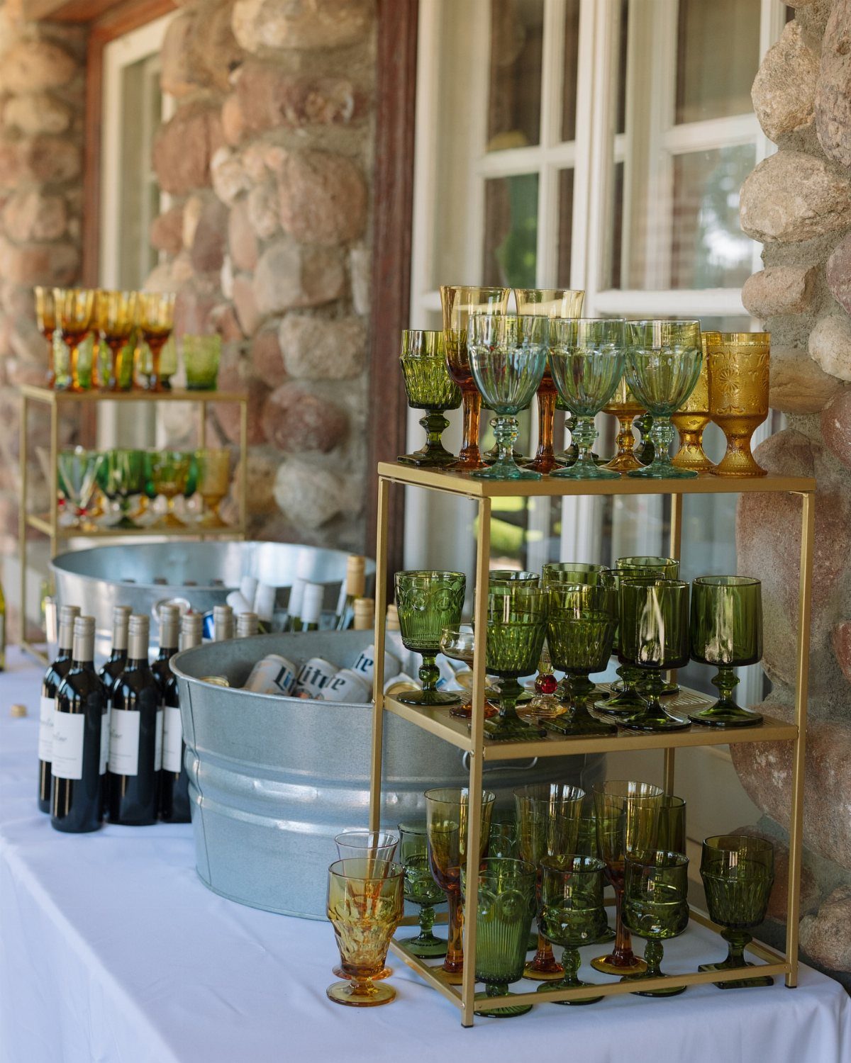 Colored vintage glassware arranged on a gold tiered shelf next to wine bottles.