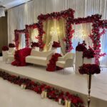 Wedding stage with white furniture and elaborate red rose floral arches and borders.