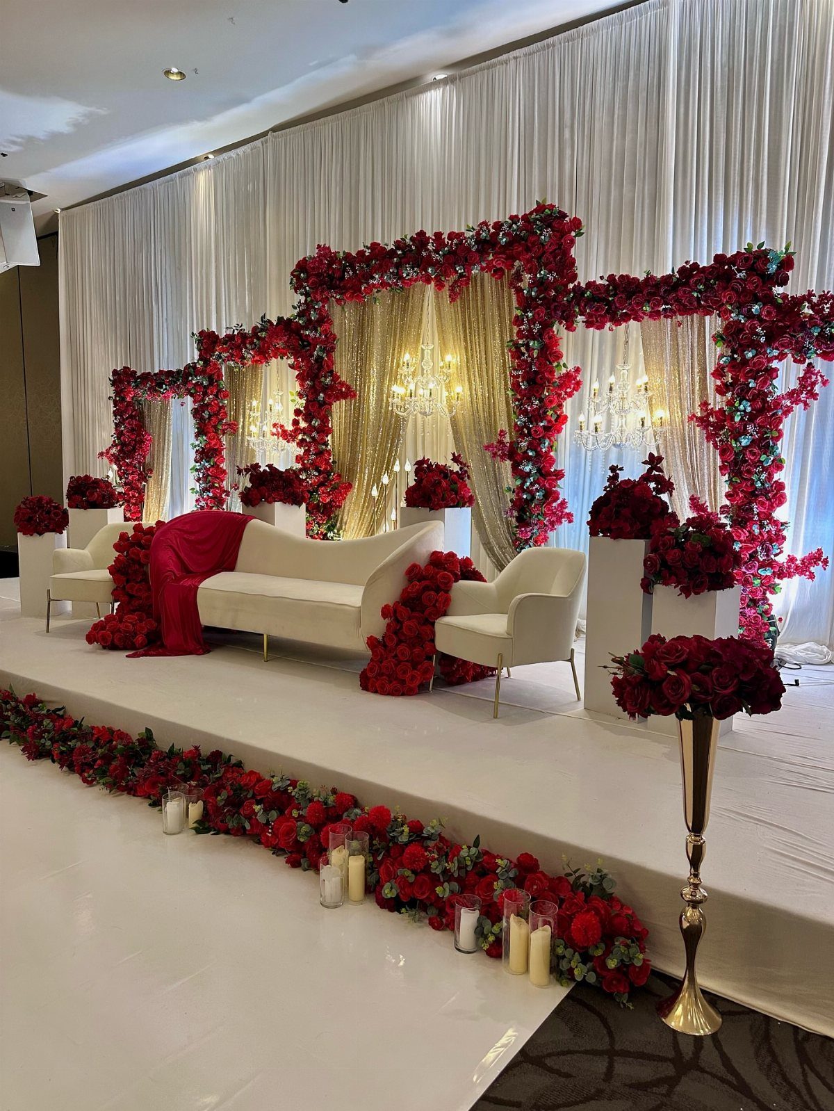 Wedding stage with white furniture and elaborate red rose floral arches and borders.