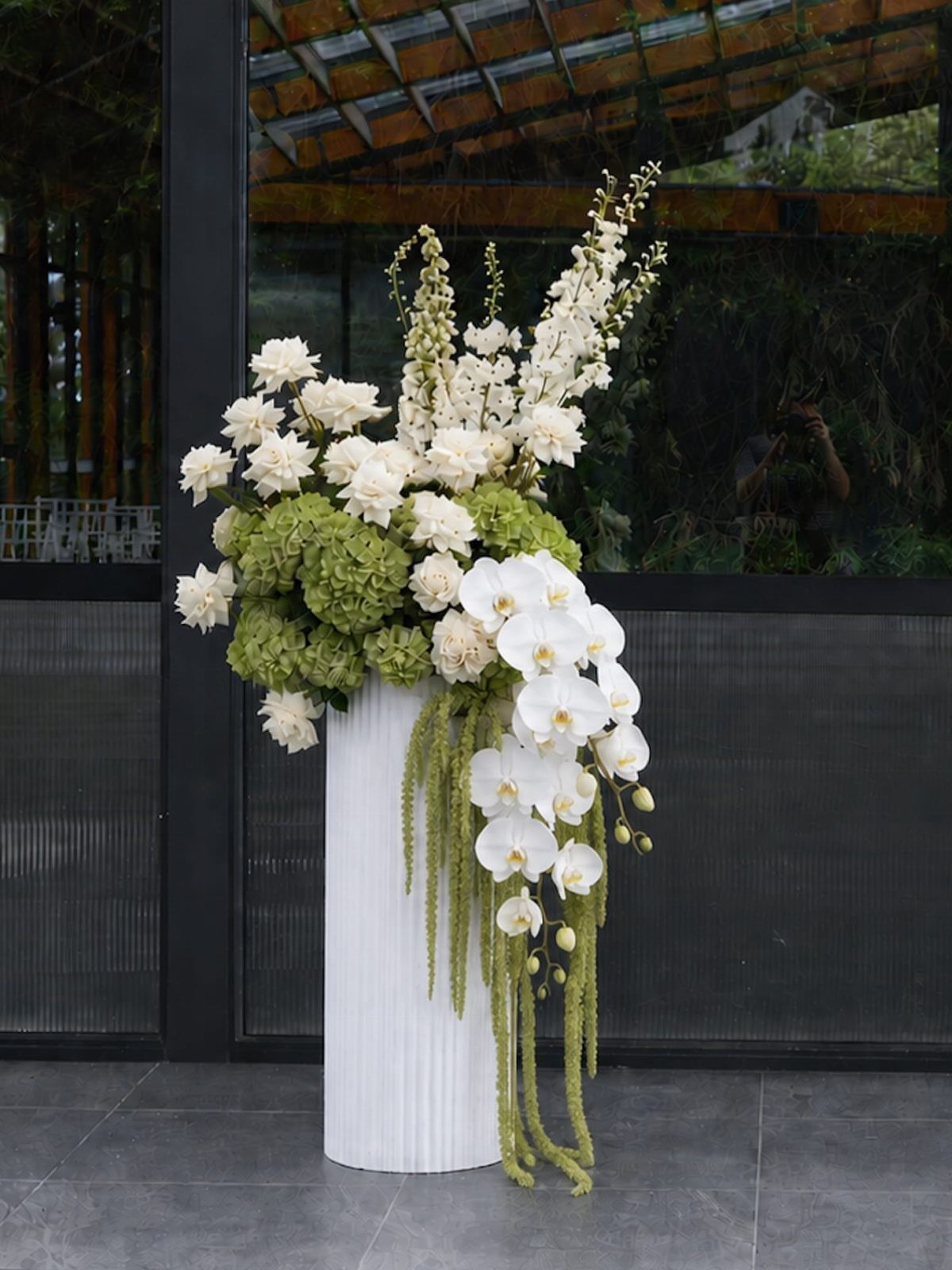 White and green floral arrangement on a white fluted pedestal for wedding decor