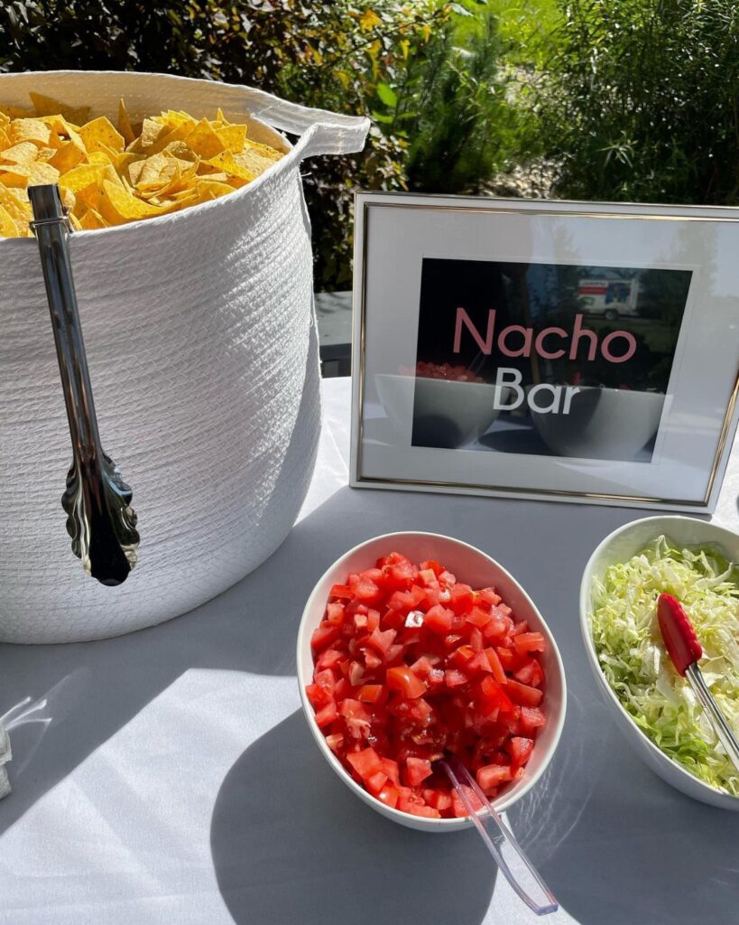 Nacho bar setup with tortilla chips, diced tomatoes, and shredded lettuce outdoors.