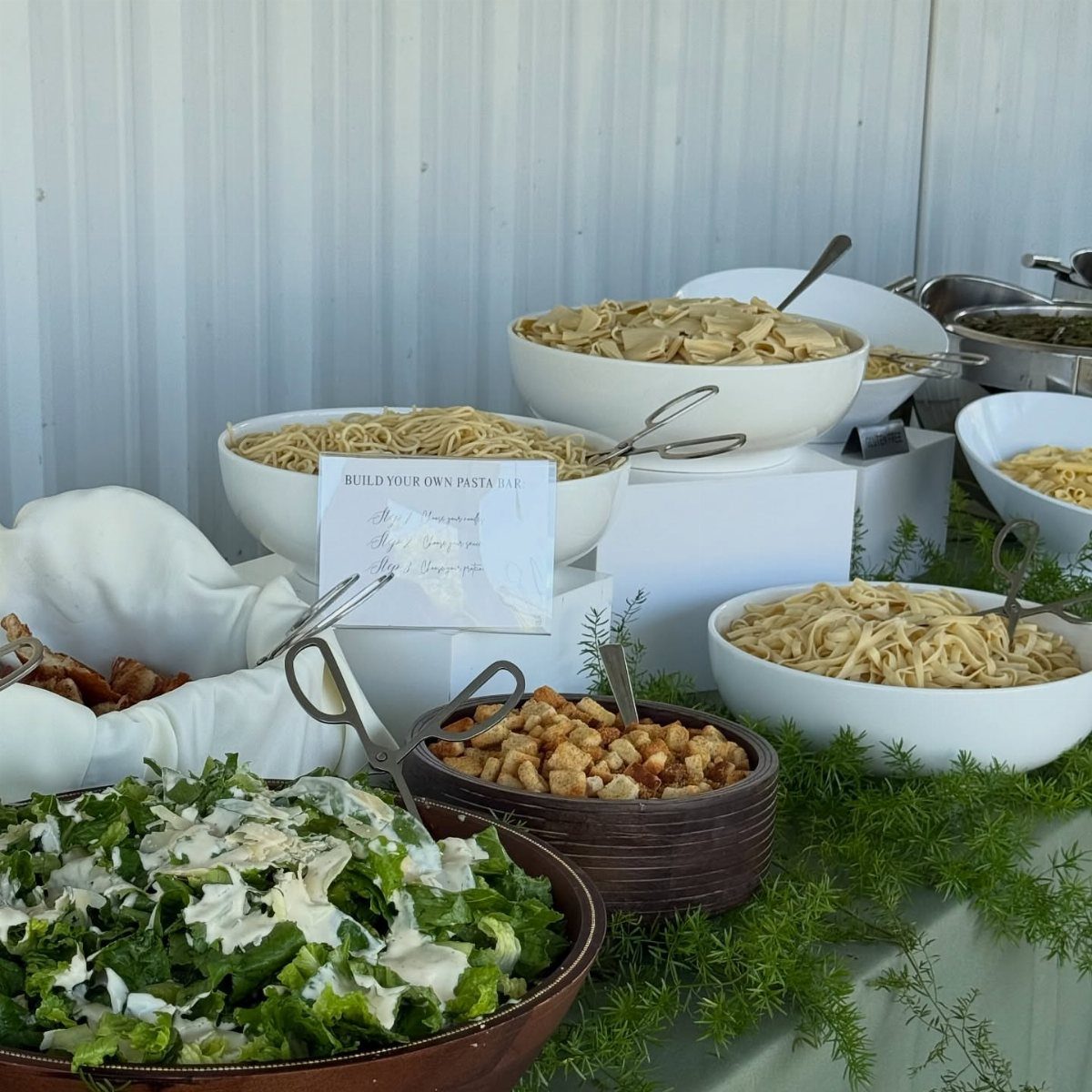 Pasta bar buffet with various noodles in white bowls and a fresh salad.
