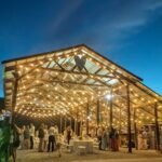 Open-air wooden barn venue illuminated by string lights for a rustic wedding reception.
