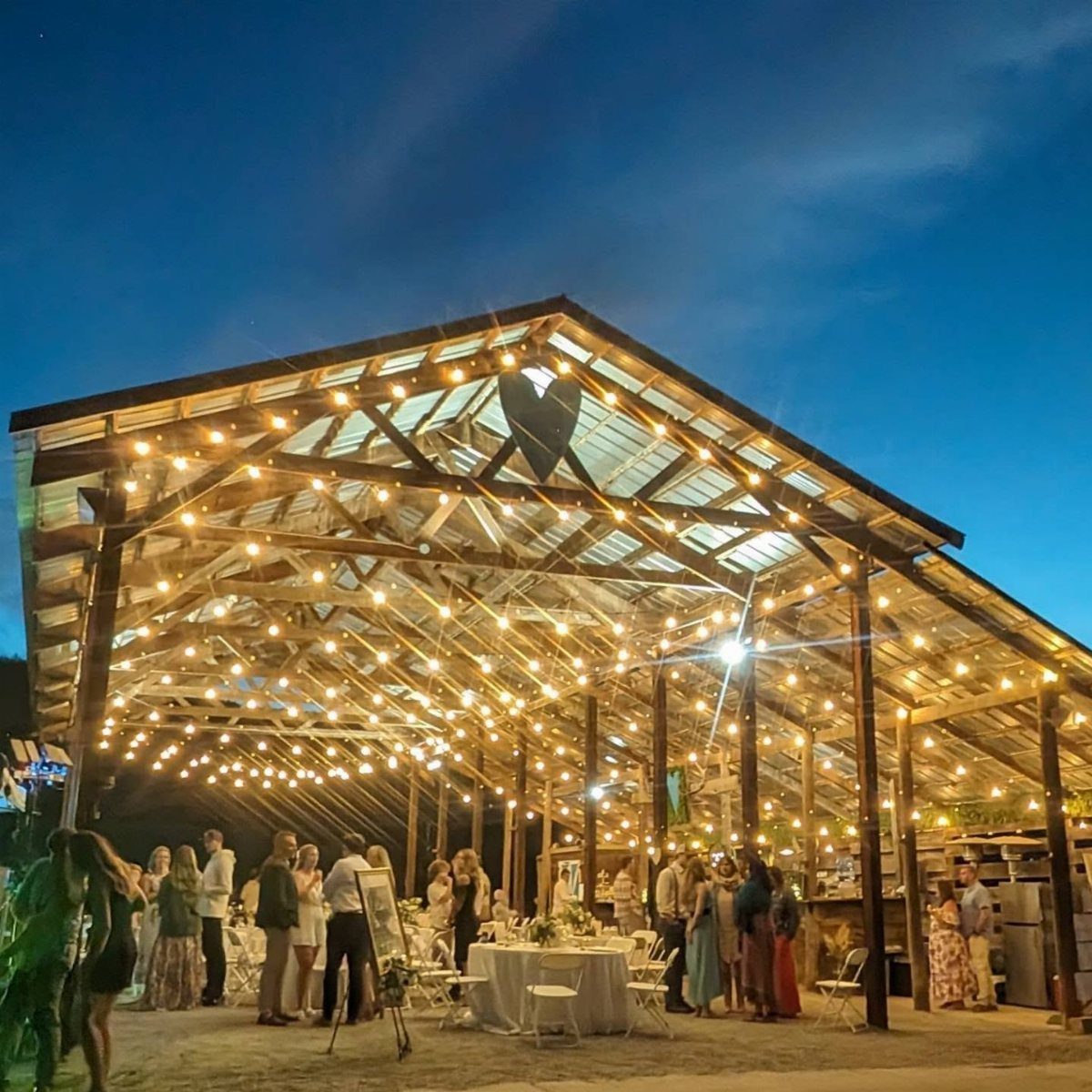 Open-air wooden barn venue illuminated by string lights for a rustic wedding reception.