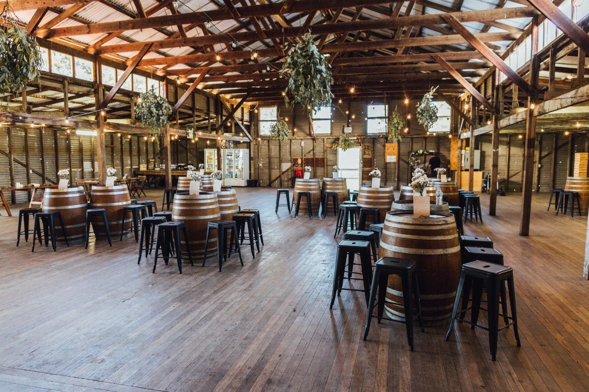 Wooden barrels used as tables with black stools in a rustic barn setting.