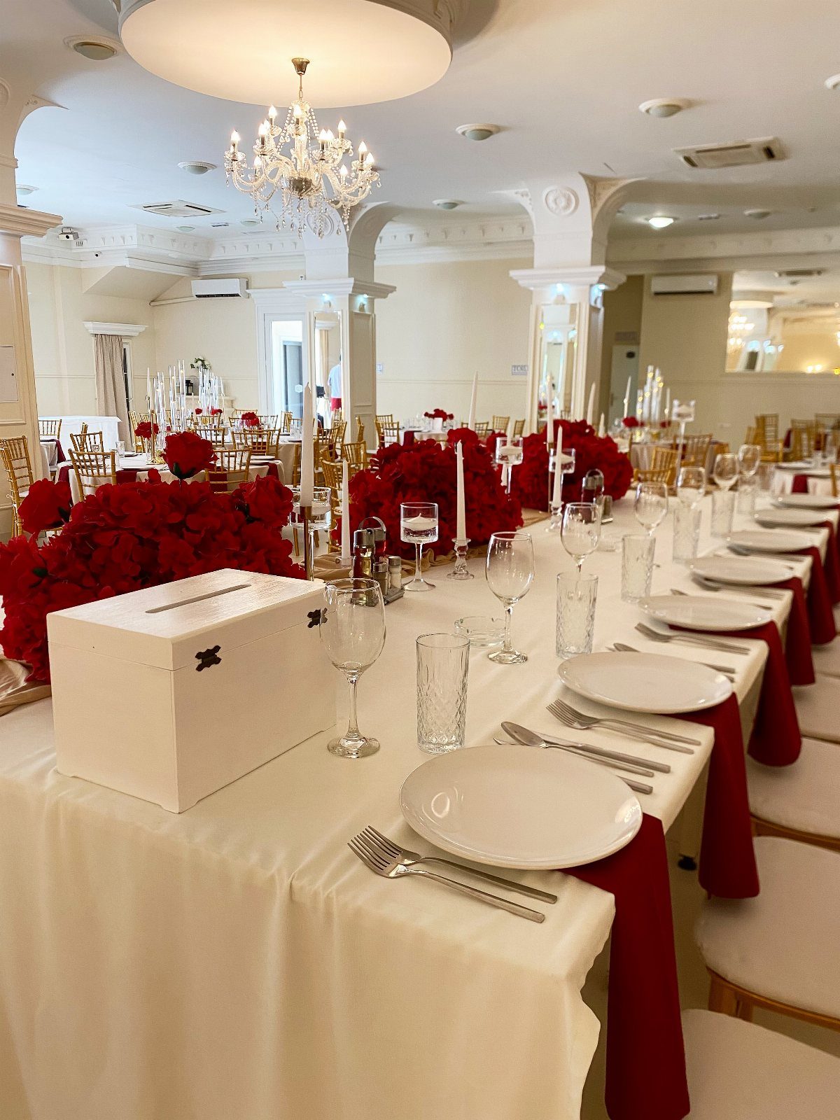Red rose centerpieces on a white wedding banquet table with red napkins.