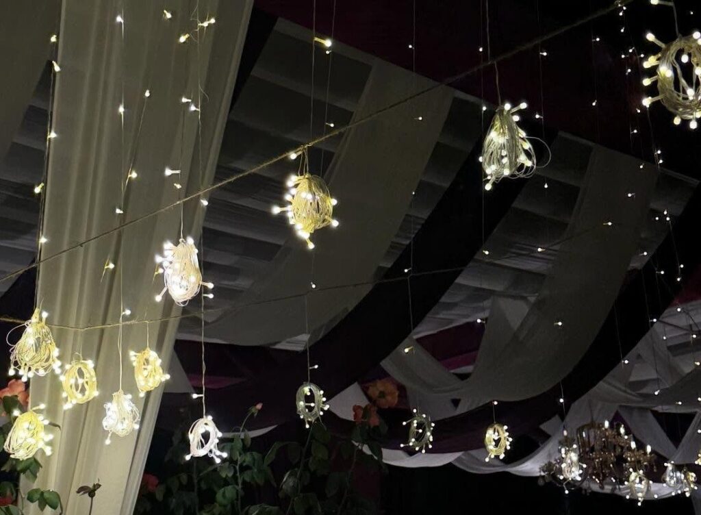 Glowing lanterns and fairy lights hanging from white fabric drapes at a wedding.
