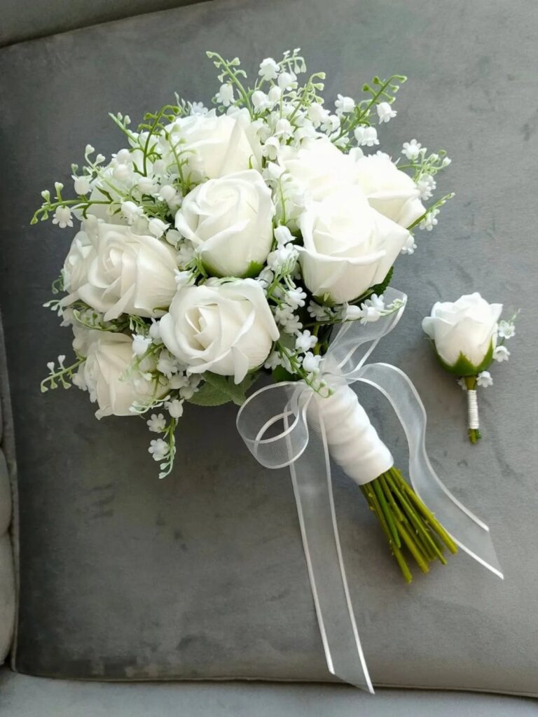 White rose bridal bouquet with baby's breath and a matching boutonniere on grey fabric