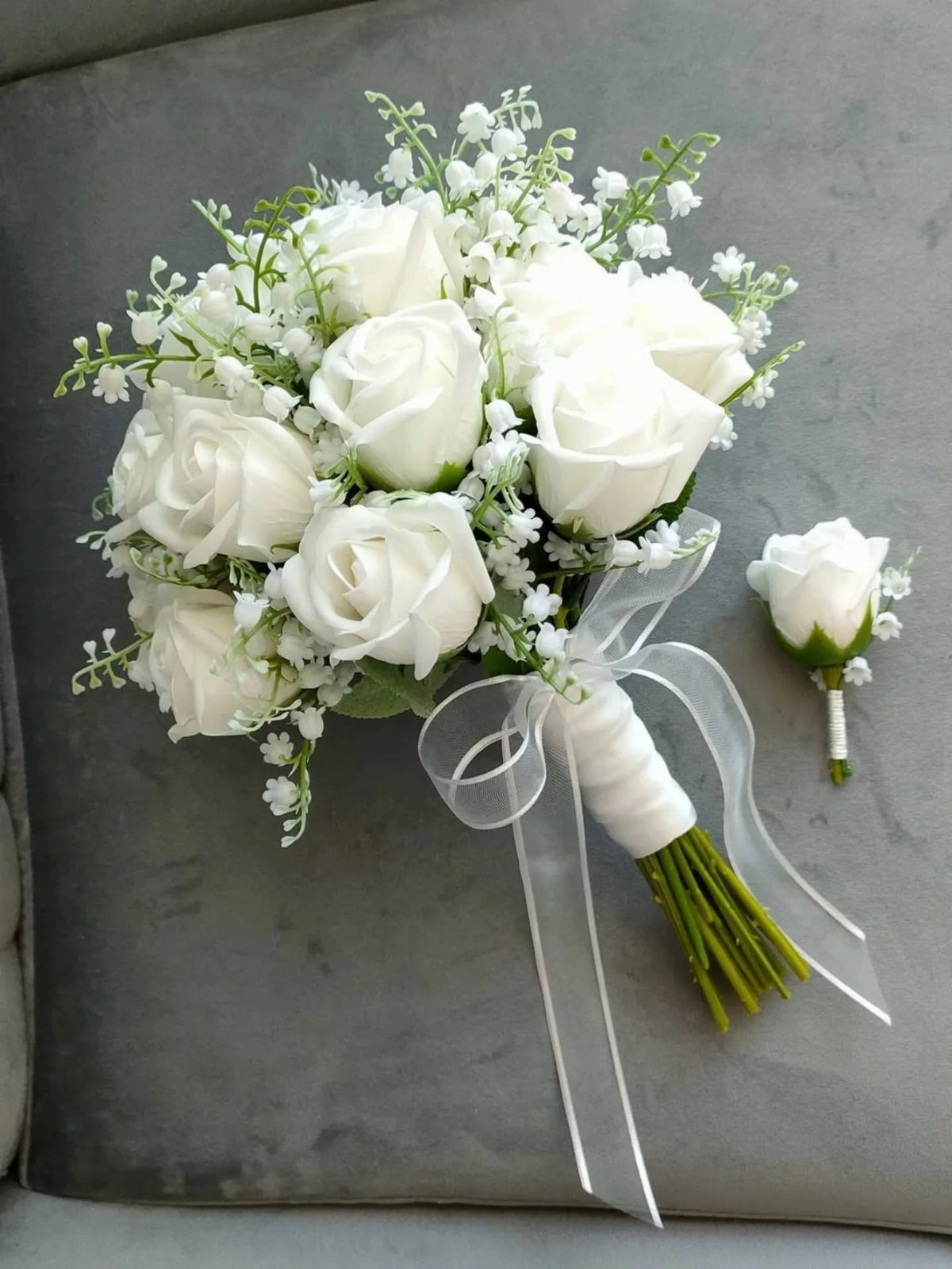 White rose bridal bouquet with baby's breath and a matching boutonniere on grey fabric