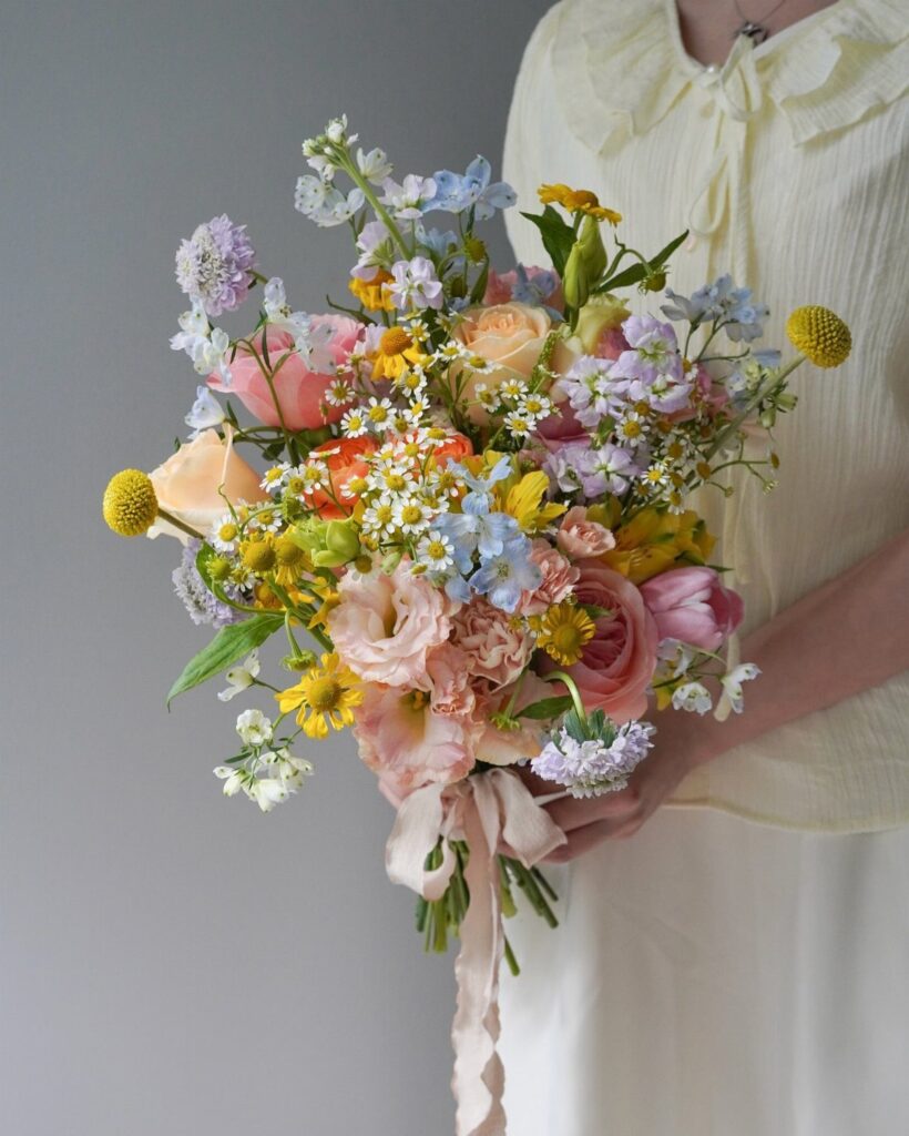 Colorful wildflower bridal bouquet with pink roses and blue flowers held by a person.