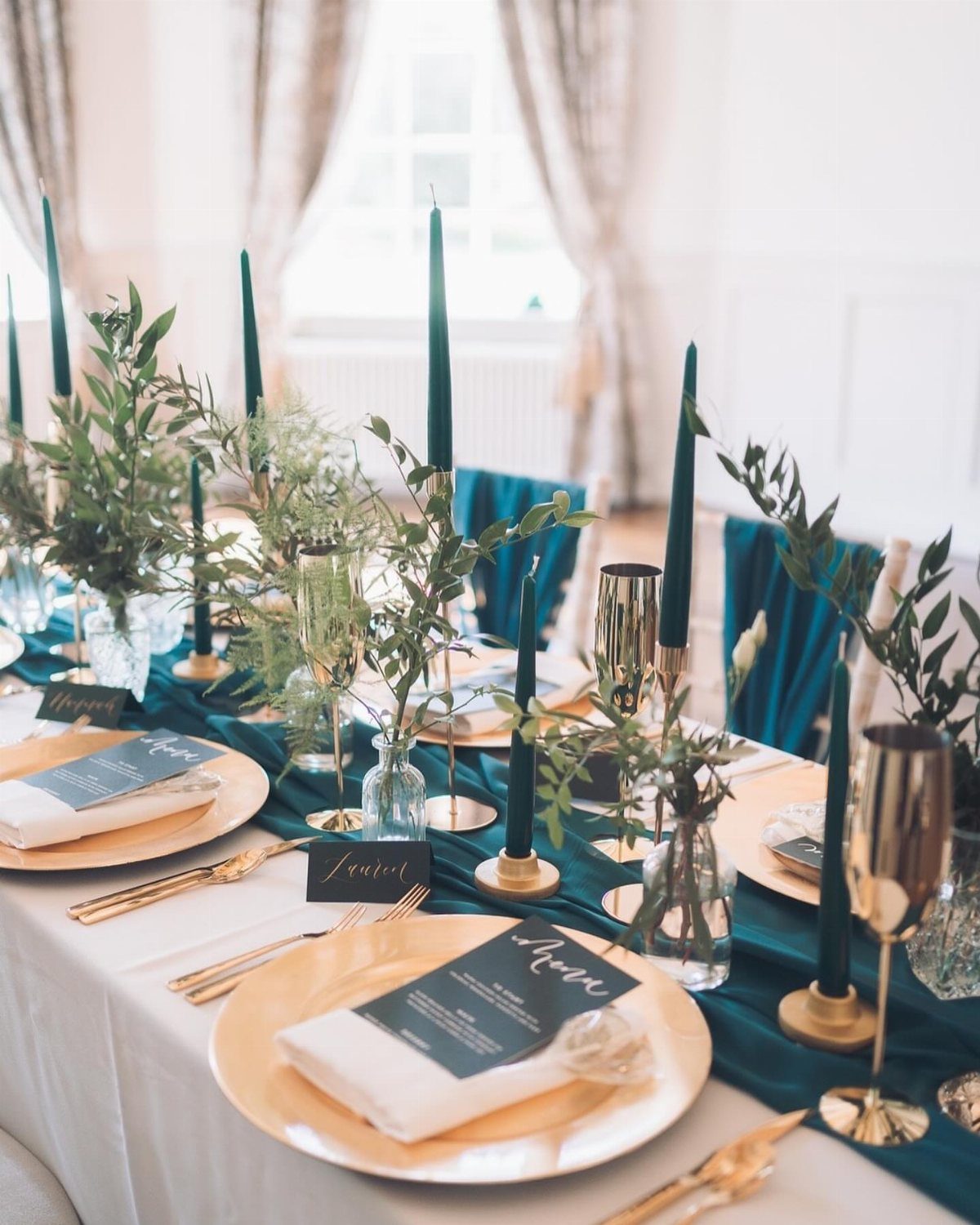 Wedding table setting with teal runner, gold plates, and tall teal taper candles.